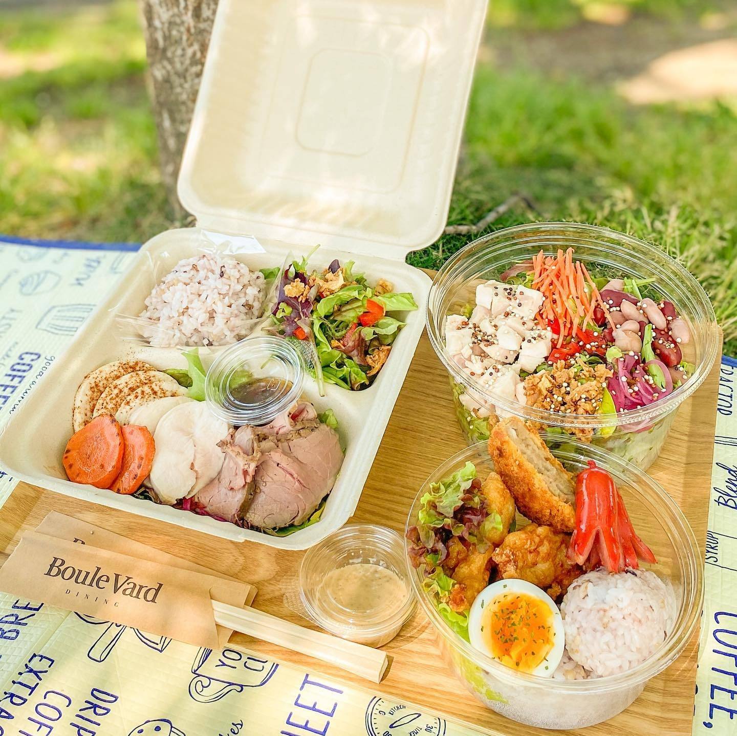 芝生の上に広げた、ローストビーフや揚げ物、サラダが詰まったお弁当