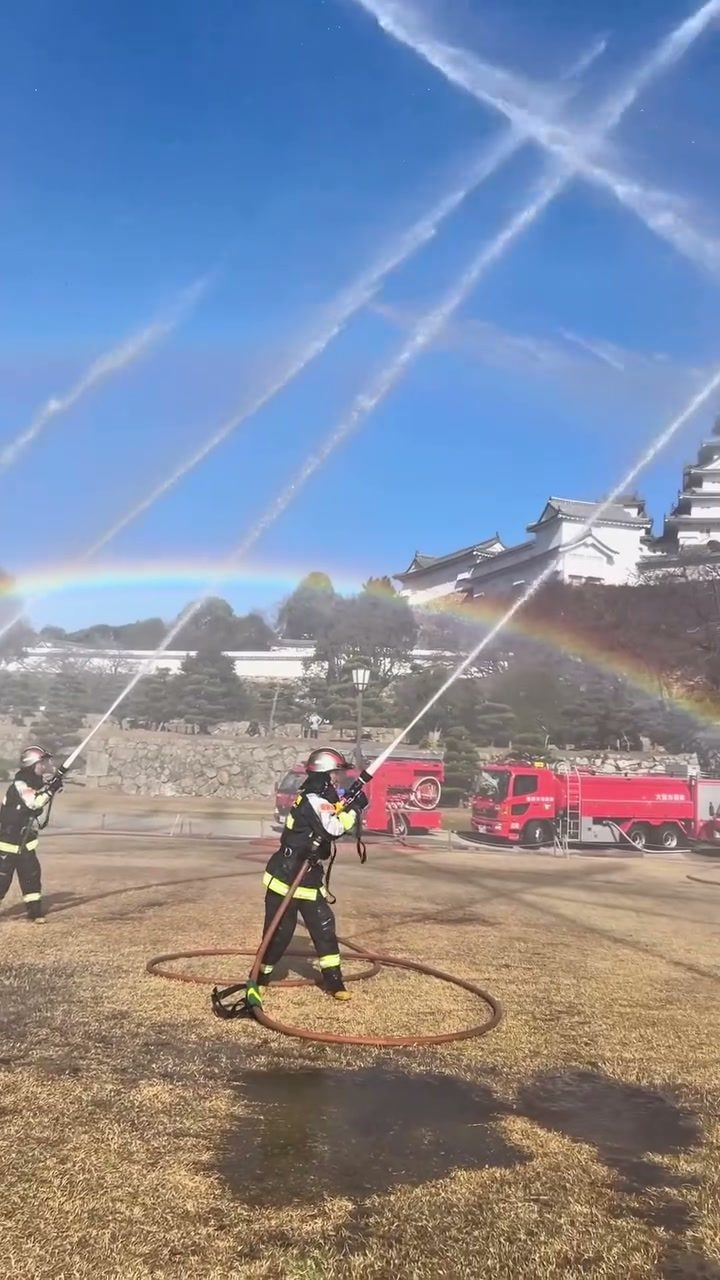 虹がかかるなかホースで放水する消防隊員