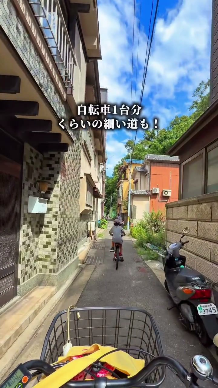 家と家の間の細い路地を自転車で進む様子