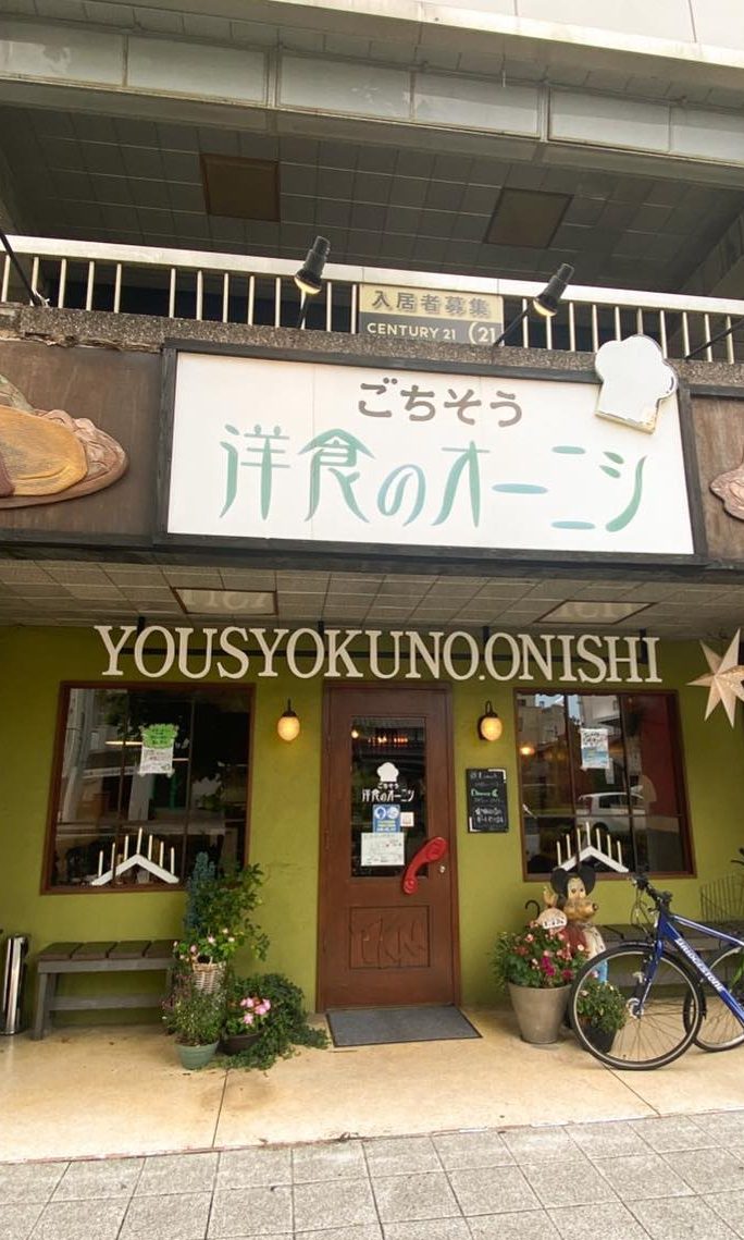 緑の外壁に看板が掛かるごちそう洋食のオーニシの外観