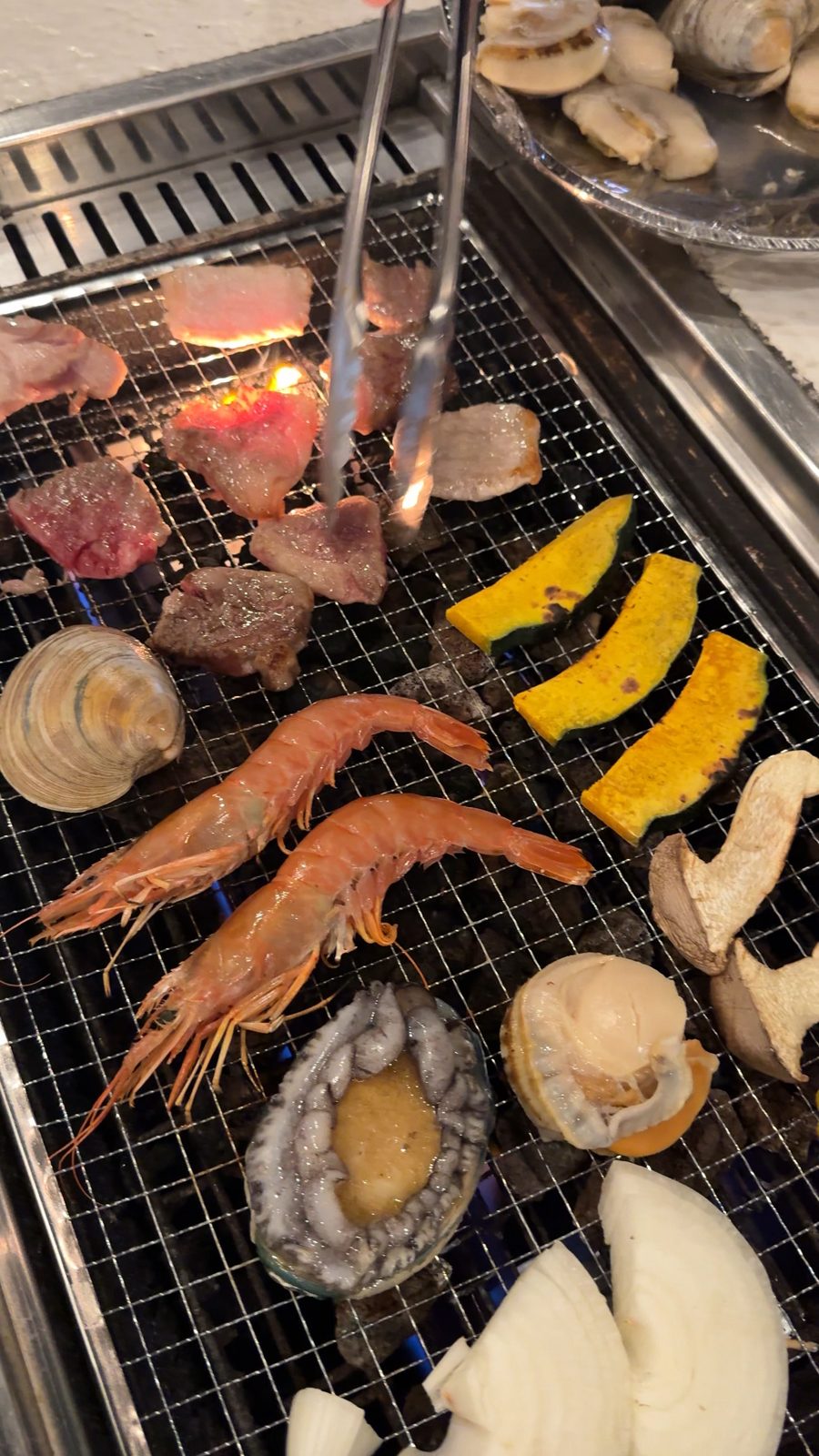 網の上で焼ける牛肉と海老、あわびなどの海鮮