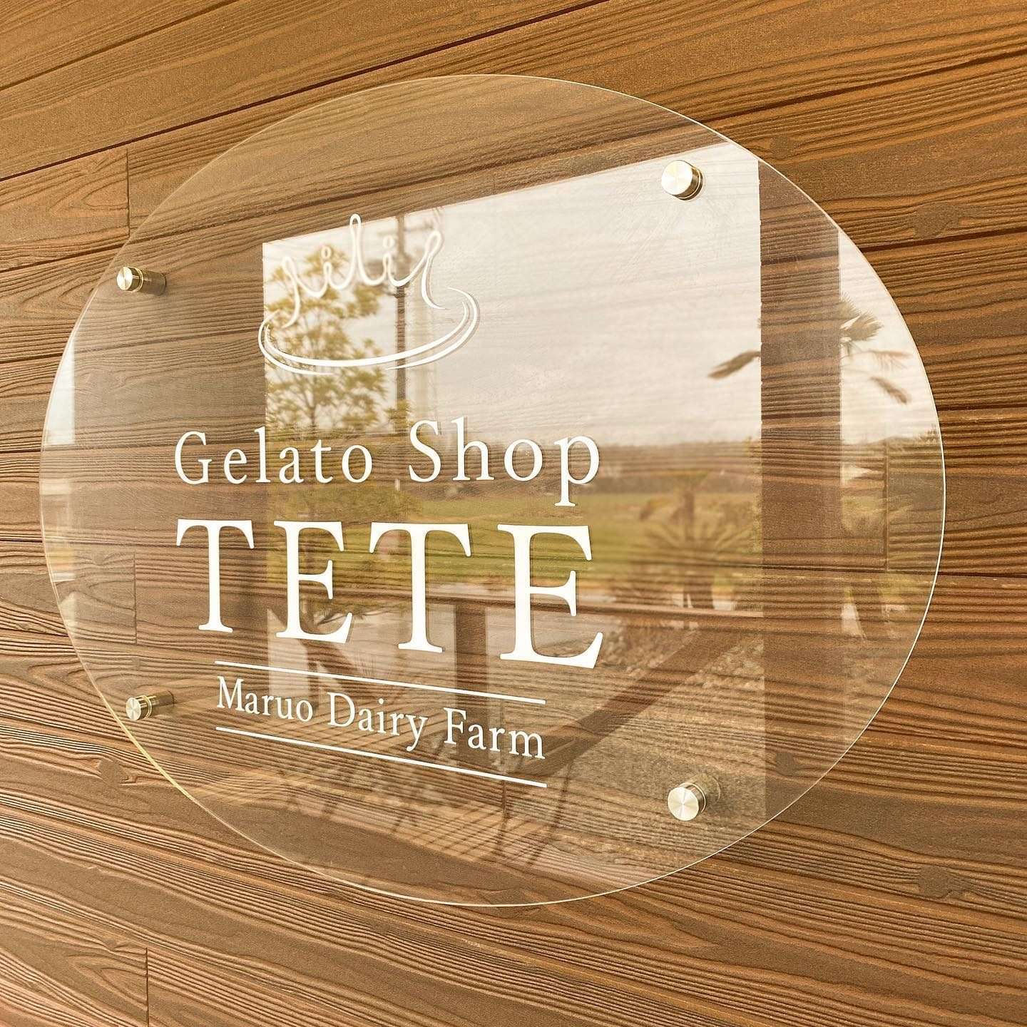 木の壁に掛けられたGelato Shop TETEの丸い看板